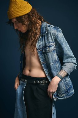 Genç adam, şık bir bereyle eşleştirilmiş bir kot ceketle moda kıyafetlerin altını çiziyor.