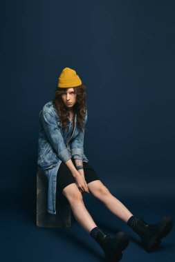 Şık giyinen yakışıklı genç bir adam yaratıcı bir stüdyoda bir kaidede dinleniyor..