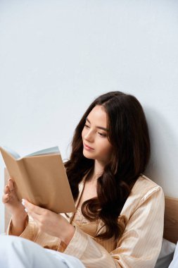 Genç bir kadın, rahat yatak odasında etrafı sükunetle çevrili bir kitap okurken rahatlıyor..