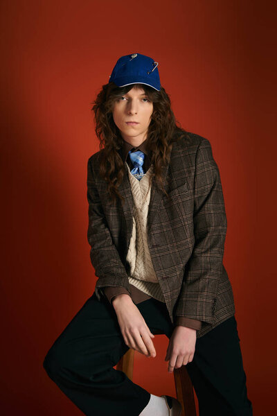 A young man sits confidently in trendy attire, radiating charm and elegance.