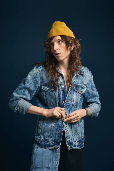 Confident young man in denim jacket and yellow beanie poses against a dark backdrop.