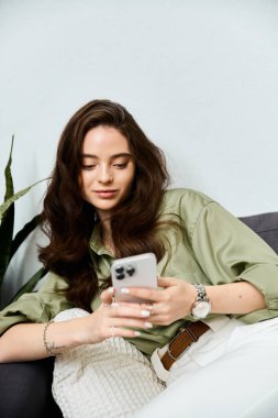 A beautiful young woman is lost in thought, interacting with her smartphone in a cozy setting. clipart