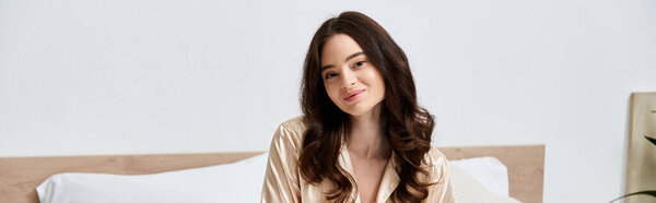 Красивая молодая женщина сидит на своей кровати, излучая радость в мягко освещенной спальне в утренние часы.