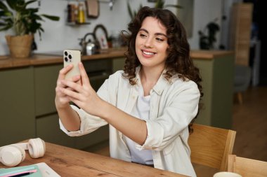 Genç bir kadın evde eğleniyor, gülümsüyor ve selfie çekiyor..