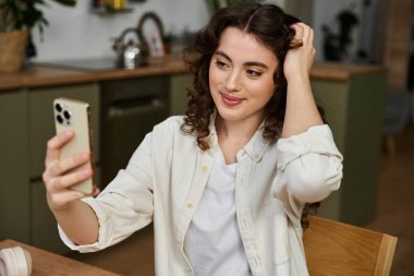 Sıcak bir gülümseme ile, güzel bir genç kadın ev konforu ile çevrili hoş bir selfie çeker..
