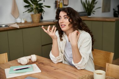 A young woman enjoys a lively conversation at her kitchen table, surrounded by plants. clipart