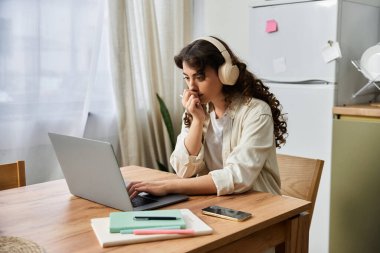 Genç bir kadın evdeki bilgisayarına odaklanmış, kulaklıklarını takmış, işine dalmış..