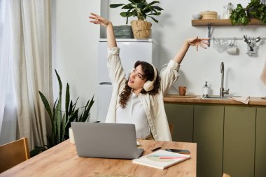 Keyifli genç bir kadın mutfak masasında çalışırken kollarını uzatıyor..