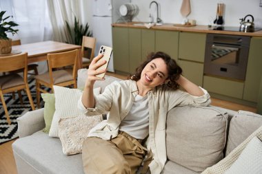 Genç bir kadın sıcak oturma odasında selfie çekerken kendini ifade eder..