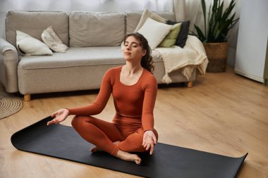 Genç bir kadın evinde meditasyonlu bir yoga seansından zevk alıyor, sükuneti kucaklıyor..