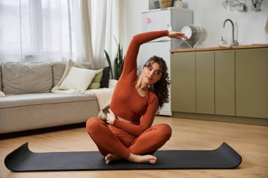 Güzel genç bir kadın şık evinde yoga minderinin üzerinde esneme egzersizleri yapıyor..