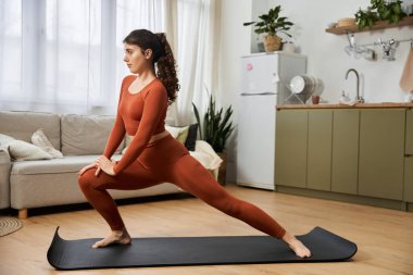 Genç bir kadın evde yoga yapıyor, gücünü ve zarafetini huzurlu bir ortamda sergiliyor..