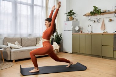 Güzel bir genç kadın evde yoga pozu veriyor, sükuneti kucaklıyor ve odaklanıyor..
