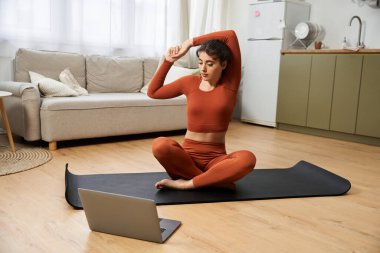 Genç bir kadın rahat bir oturma odasında yoga yapıyor, nefesine ve hareketlerine odaklanıyor..