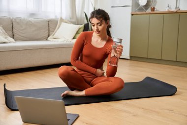Güzel, genç bir kadın yoga minderinde otururken susuzluktan zevk alıyor..