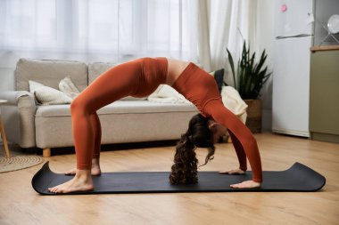 Genç bir kadın evde yoga yapıyor, kendini rahat hissederken esneklik ve odaklanma gösteriyor..