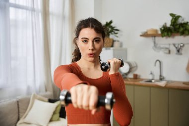 Evde egzersiz yapan bu genç kadın ağırlık kaldırırken gücünü ve kararlılığını gösteriyor..