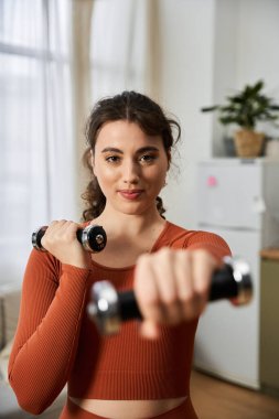 Focused woman exercises at home, lifting weights with determination and strength in a modern room. clipart