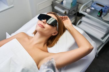 Genç bir kadın şık bir klinikte lazer kılı temizleme tedavisi görürken rahatlıyor..