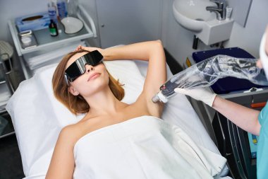 Genç bir kadın bir güzellik kliniğinde acısız bir lazer epilasyon seansından zevk alıyor. Kusursuz bir cilt garantisi veriyor..