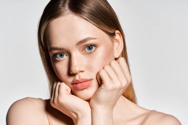 Çarpıcı mavi gözleri olan genç bir kadın zarif pozlar veriyor. Yumuşak ışıkta elleri yüzüne yakın duruyor.