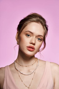 Şık giyinmiş ve zarif aksesuarları olan çekici genç bir kadın pembe bir arka fona karşı duruyor..