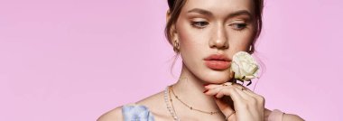 Genç ve güzel bir kadın zarif bir şekilde pembe bir zemine karşı poz veriyor, şık kıyafetlerini büyütüyor..