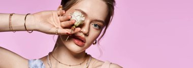 Genç bir kadın gözünün yanında bir çiçek tutuyor, bahar kıyafetleri içinde zarafet saçıyor..