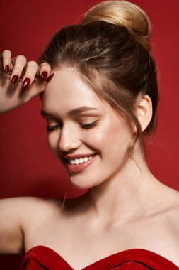 Genç bir kadın, çarpıcı bir kırmızı zemine zarif bir şekilde gülümseyerek güzellik ve tarz yayar..