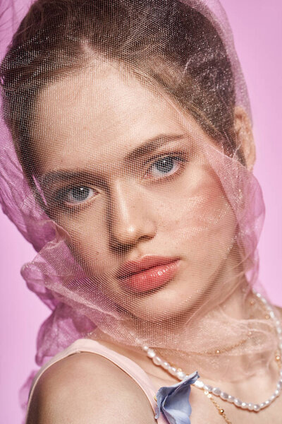 Потрясающая молодая женщина с очаровательными чертами лица изящно позирует на мягком розовом фоне.