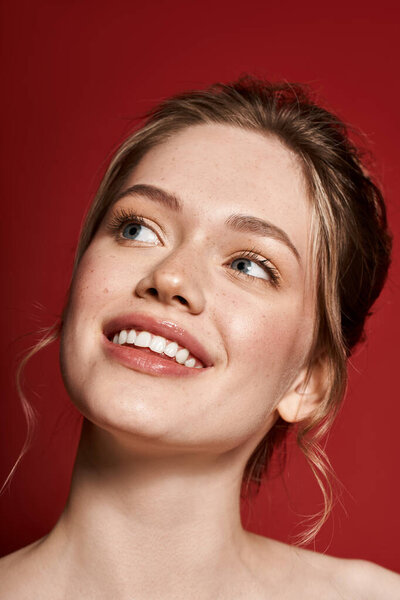 Стильная женщина показывает свою природную красоту с улыбкой на ярком красном фоне.