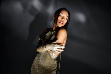 Genç bir kadın zarif ve sofistike altın bir elbise ve şık eldivenler giyer..