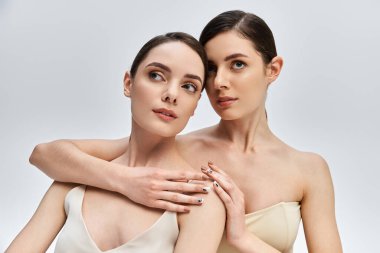 İki güzel kız kardeş zarif bir şekilde poz verir, yumuşak ışıkta güzelliklerini ve bağlarını sergilerler..