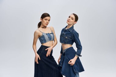 İki güzel ikiz kız kardeş şık kot kıyafetlerle, zarafet ve cazibe saçarak rahatça poz veriyorlar..