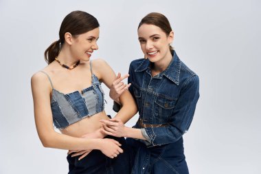 İki şık kız kardeş güzel bir anı paylaşıyor, kot elbiseleriyle birbirlerine yakınlar..