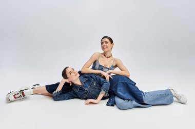 İki güzel ikiz yerde rahatlar, zarif bir şekilde gülümseyerek kostüm giyerek poz verirler..