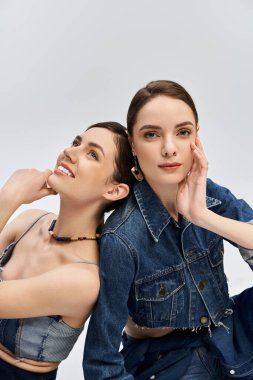 İkiz kız kardeşler şık kotların içinde neşeli bir şekilde poz verirler, göz alıcı gülümsemelerini sergilerler..