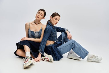 Parlak bir stüdyoda iki şık kadın kot giysisi ve modern spor ayakkabısı..