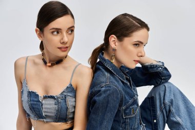 Two beautiful twin women model trendy denim outfits, exuding elegance and charm in a sleek backdrop. clipart