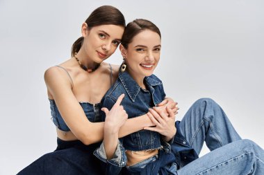 İki güzel ikiz kadın şık kotlar giyerken neşeli bir etkileşimi paylaşıyor..