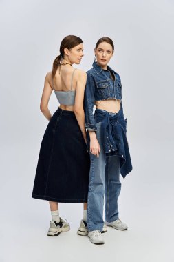 İki güzel kız kardeş arka arkaya poz veriyor, stüdyoda eşsiz kot kıyafetlerini gösteriyorlar..