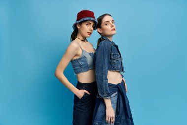 İki güzel kadın arka arkaya parlak bir şekilde poz verirken şık kot elbiseler sergiliyor..