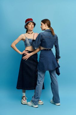 İki güzel ikiz kardeş benzersiz kot kıyafetlerini çarpıcı bir mavi atmosferde sergiliyorlar..