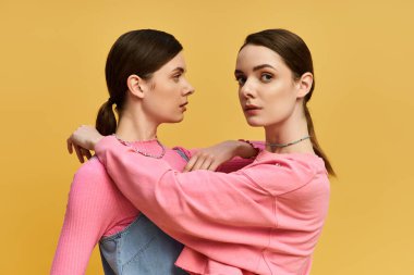 İki güzel kız kardeş canlı sarı bir arkaplanda poz veriyor, güzelliklerini sergiliyorlar..