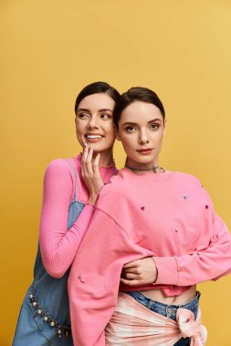 İki güzel ikiz kardeş neşeli bir şekilde canlı sarı bir arka plana poz veriyor, mutluluk saçıyorlar..