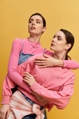 Pembe elbiseli iki ikiz kardeş neşeli bir ortamda birlikte poz veriyorlar..