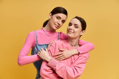 İki güzel kız kardeş, neşeli bir ortamda şık kıyafetler giyerek birbirlerine yakınlıklarını gösteriyorlar..