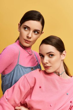 İki güzel ikiz kardeş tarzlarını sergiliyorlar, parlak sarı bir zemin üzerinde ışıl ışıl parlıyorlar..