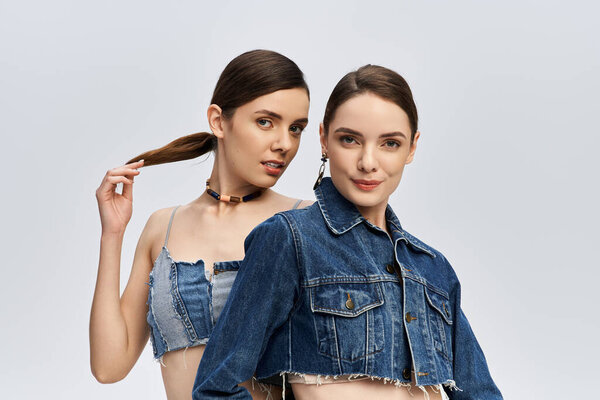 Сестры-близнецы изящно позируют в стильных джинсах, излучающих шарм и элегантность.