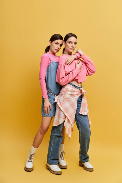 Two pretty sisters stand confidently together, showcasing their stylish outfits in a vivid setting.